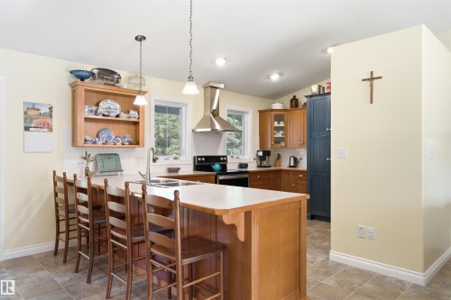 Kitchen with wood-finish cabinetry, a peninsula with bar seating, and a stainless steel range hood - 59125 Range Road 102, Rural St. Paul County, AB - Indoor