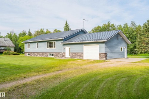 Light blue siding exterior featuring a stone veneer foundation accent, a dark metal roof, and an attached garage with a white overhead door - 59125 Range Road 102, Rural St. Paul County, AB - Outdoor