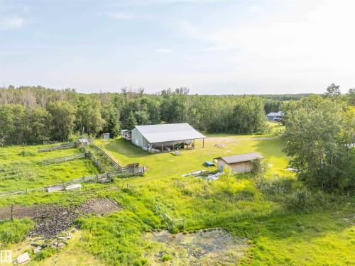 Expansive rural property featuring a large light-colored shop with two attached open-sided structures, a smaller wood-sided outbuilding, fenced pasture areas, and extensive green space surrounded by mature trees - 59125 Range Road 102, Rural St. Paul County, AB - Outdoor With View