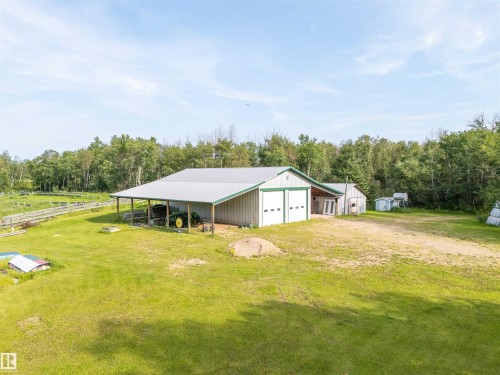 Large Shop structure featuring a light gray metal roof, two white garage doors with green trim, and an attached covered lean-to area - 59125 Range Road 102, Rural St. Paul County, AB - Outdoor