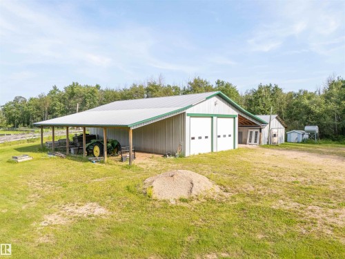 Metal-sided outbuilding with two roll-up garage doors, a covered side extension, and a pitched metal roof - 59125 Range Road 102, Rural St. Paul County, AB - Outdoor With Deck Patio Veranda