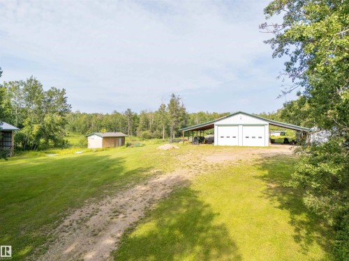 Expansive green space featuring a large shop with two roll-up garage doors, an extended covered carport, and a smaller auxiliary structure - 59125 Range Road 102, Rural St. Paul County, AB - Outdoor