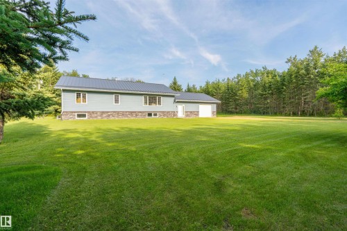 Spacious green lawn surrounding a light blue siding home with a dark metal roof, stone foundation, and attached garage - 59125 Range Road 102, Rural St. Paul County, AB - Outdoor