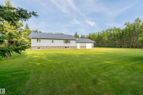 Expansive green lawn bordering a light blue siding residence with a dark metal roof, stone veneer foundation, and an attached garage - 59125 Range Road 102, Rural St. Paul County, AB - Outdoor