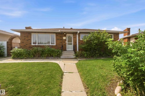 Welcoming brick ranch home featuring a manicured front lawn with mature landscaping, a centered concrete walkway, large front-facing windows, and a covered entry portico - 8031 135A Avenue Nw, Edmonton, AB - Outdoor