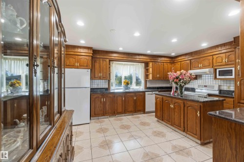 Kitchen featuring extensive wood cabinetry, white appliances, a center island with a dark countertop, and tiled flooring - 8031 135A Avenue Nw, Edmonton, AB - Indoor Photo Showing Kitchen