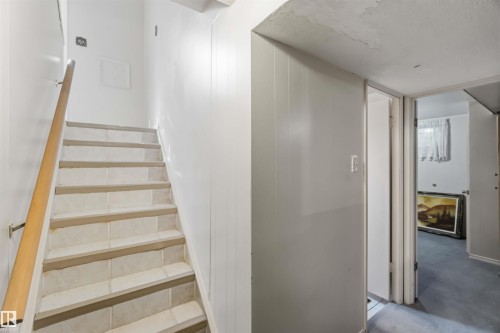 Staircase with light-toned tile treads and a wood-finish handrail, complemented by vertical paneling - 8031 135A Avenue Nw, Edmonton, AB - Indoor Photo Showing Other Room