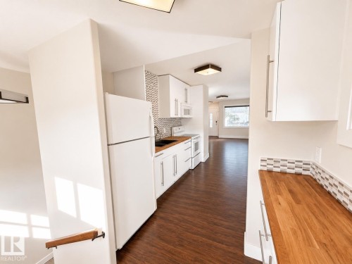 Kitchen featuring wood-finish flooring, white cabinetry, wood countertops, and a tiled backsplash - 11934 64 Street Nw, Edmonton, AB - Indoor Photo Showing Kitchen