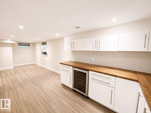 Recessed lighting, wood-finish flooring, white cabinetry with contemporary pulls, wood countertops, and a beverage refrigerator - 11934 64 Street Nw, Edmonton, AB - Indoor Photo Showing Kitchen