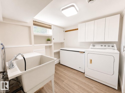 Utility room featuring a utility sink, light wood-finish flooring, built-in shelving, and white upper cabinetry - 11934 64 Street Nw, Edmonton, AB - Indoor Photo Showing Laundry Room