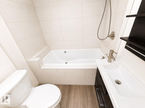 Integrated bathtub with tiled surround, wall-mounted shower fixture, modern vanity with rectangular sink, brushed nickel faucet, and wood-finish flooring - 11934 64 Street Nw, Edmonton, AB - Indoor Photo Showing Bathroom