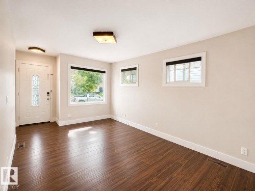 Bright, open living space featuring rich wood-finish flooring throughout, multiple windows with black-trimmed frames flooding the room with natural light, recessed ceiling fixtures, and a cream-painted wall palette - 11934 64 Street Nw, Edmonton, AB - Indoor Photo Showing Other Room