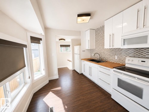 Kitchen featuring white cabinetry, wood-finish countertops, geometric tile backsplash, and a double basin sink - 11934 64 Street Nw, Edmonton, AB - Indoor Photo Showing Kitchen With Double Sink