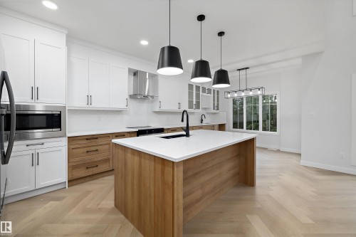 Modern kitchen featuring white cabinetry, light wood-finish flooring, a central island with a white countertop, and stainless steel appliances - 971 Elderberry Landing Nw, Edmonton, AB - Indoor Photo Showing Kitchen
