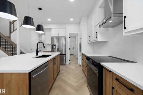 Kitchen featuring a large island with sink, herringbone wood-finish flooring, white cabinetry, stainless steel appliances, and a range hood - 971 Elderberry Landing Nw, Edmonton, AB - Indoor Photo Showing Kitchen With Upgraded Kitchen