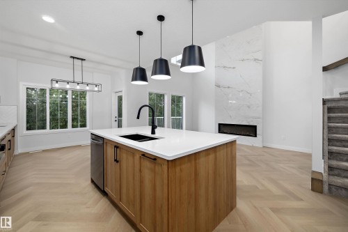 Open-concept living area with wood-finish flooring, a contemporary fireplace, and a kitchen island with a built-in sink and dishwasher - 971 Elderberry Landing Nw, Edmonton, AB - Indoor Photo Showing Kitchen With Double Sink
