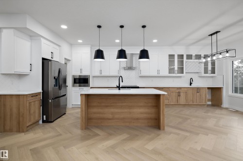 Spacious kitchen featuring an island with a light-toned wood-finish base, white countertops, and herringbone-patterned wood-finish flooring - 971 Elderberry Landing Nw, Edmonton, AB - Indoor Photo Showing Kitchen