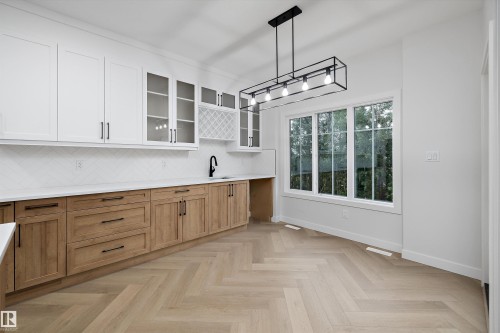 Contrasting cabinetry with white upper and wood-finish lower cabinets, stone countertops, a herringbone pattern wood-finish floor, a large multi-pane window, and a linear black chandelier - 971 Elderberry Landing Nw, Edmonton, AB - Indoor