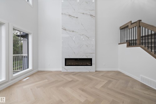 Herringbone wood-finish flooring, two-story accent wall with electric fireplace, large windows, wood and metal staircase - 971 Elderberry Landing Nw, Edmonton, AB - Indoor Photo Showing Living Room With Fireplace