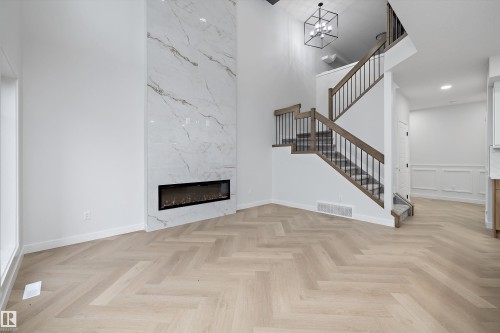 Two-story living area with herringbone wood-finish flooring, a full-height tiled fireplace surround, and a linear electric fireplace - 971 Elderberry Landing Nw, Edmonton, AB - Indoor With Fireplace