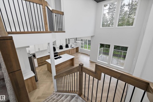 Two-story architectural design, high ceilings, large windows, wood-finish flooring with a herringbone pattern, and a modern kitchen with a central island - 971 Elderberry Landing Nw, Edmonton, AB - Indoor Photo Showing Other Room