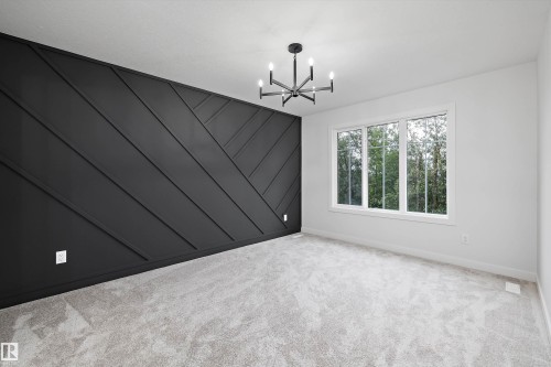 Accent wall with geometric paneling, contemporary chandelier, large picture window, and light-toned carpeting - 971 Elderberry Landing Nw, Edmonton, AB -  Photo Showing Other Room