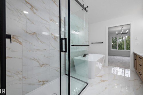 Glass-enclosed shower with black trim, freestanding soaking tub, wood-finish vanity with countertop, and large format floor tiles - 971 Elderberry Landing Nw, Edmonton, AB - Indoor Photo Showing Bathroom