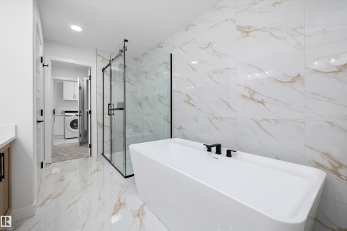 Freestanding soaking tub with matte black fixtures, glass-enclosed shower, and large format wall and floor tiling - 971 Elderberry Landing Nw, Edmonton, AB - Indoor Photo Showing Bathroom