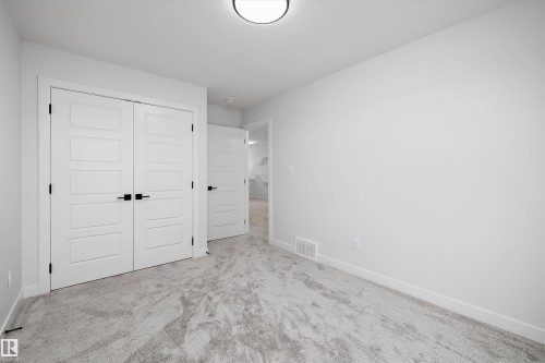 Recessed ceiling light fixture, light gray carpeting, white painted walls, white paneled doors with black hardware, and white trim - 971 Elderberry Landing Nw, Edmonton, AB - Indoor Photo Showing Other Room