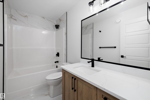 Bathroom featuring a built-in tub with a tile surround, wood-finish vanity with a white countertop, undermount sink, and matte black hardware - 971 Elderberry Landing Nw, Edmonton, AB - Indoor Photo Showing Bathroom