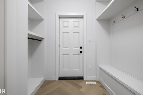 Entryway featuring wood-finish flooring with a herringbone pattern, a paneled door with black hardware, built-in shelving, a built-in bench, and black coat hooks - 971 Elderberry Landing Nw, Edmonton, AB - Indoor