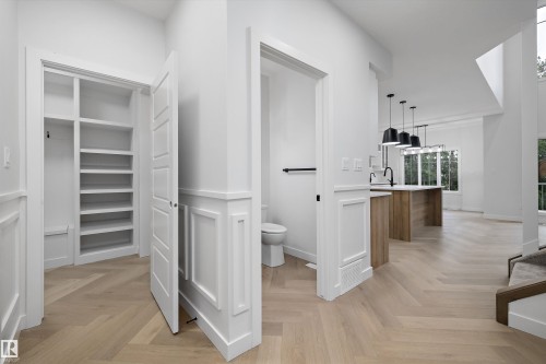Herringbone wood-finish flooring, wainscoting, built-in shelving, kitchen island with integrated sink, and contemporary pendant lighting fixtures - 971 Elderberry Landing Nw, Edmonton, AB - Indoor