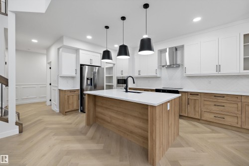 Modern kitchen featuring a large center island with a white countertop, two-tone cabinetry, stainless steel appliances, and wood-finish herringbone flooring - 971 Elderberry Landing Nw, Edmonton, AB - Indoor Photo Showing Kitchen With Upgraded Kitchen
