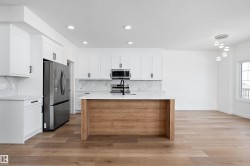 Kitchen featuring white shaker-style cabinetry, a wood-finish island with a white countertop, stainless steel appliances, and wood-finish flooring - 