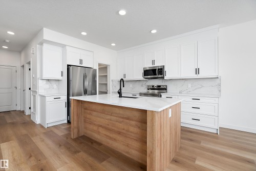 Modern kitchen featuring a wood-finish island, white cabinetry, integrated stainless steel appliances, and light-toned flooring - 1763 Crossbill Loop Nw, Edmonton, AB - Indoor Photo Showing Kitchen With Upgraded Kitchen