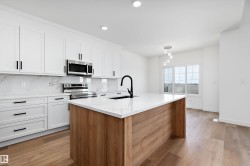 Modern kitchen featuring white cabinetry, a wood-finish island with a white countertop, and stainless steel appliances - 