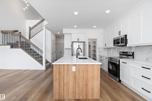 Kitchen featuring white cabinetry, stainless steel appliances, a center island with light wood-finish paneling, and a light-toned wood-finish flooring - 1763 Crossbill Loop Nw, Edmonton, AB - Indoor Photo Showing Kitchen With Upgraded Kitchen