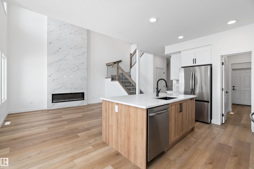 Soaring ceiling with a full-height marble-look fireplace - 1763 Crossbill Loop Nw, Edmonton, AB - Indoor Photo Showing Kitchen