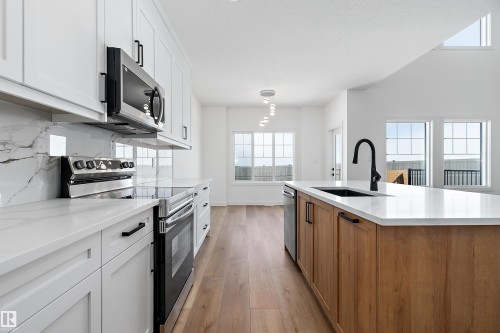 Kitchen featuring white shaker cabinetry, stainless steel appliances, marble-look backsplash, wood-finish flooring, and a central island with a contrasting wood-finish base and integrated sink - 1763 Crossbill Loop Nw, Edmonton, AB - Indoor Photo Showing Kitchen With Upgraded Kitchen
