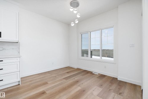 White cabinetry with black hardware, white quartz countertop with matching backsplash, wood-finish flooring, contemporary ceiling light fixture, and a large window - 1763 Crossbill Loop Nw, Edmonton, AB - Indoor Photo Showing Other Room