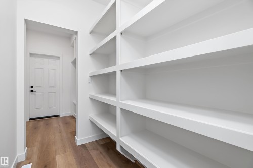 Extensive built-in shelving, wood-finish flooring, white paneled door, and white painted walls - 1763 Crossbill Loop Nw, Edmonton, AB - Indoor With Storage