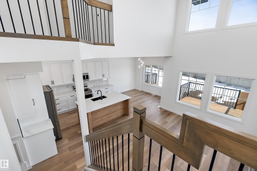Two-story living area with high ceilings, wood-finish flooring, a contemporary kitchen, and a wooden deck - 1763 Crossbill Loop Nw, Edmonton, AB - Indoor Photo Showing Other Room