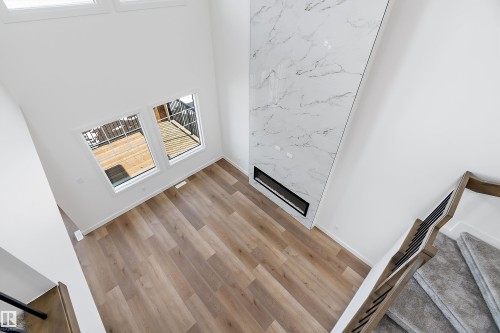 Double-height living area featuring wood-finish flooring, a contemporary fireplace with a stone-look surround, and a carpeted staircase with a dark metal and wood railing - 1763 Crossbill Loop Nw, Edmonton, AB - Indoor Photo Showing Other Room