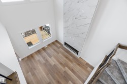 Double-height living area featuring wood-finish flooring, a contemporary fireplace with a stone-look surround, and a carpeted staircase with a dark metal and wood railing - 