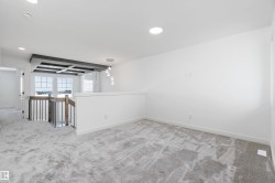 Open loft area featuring recessed lighting, a decorative ceiling treatment, a modern pendant light fixture, and a stairway with a wood newel post and metal balusters - 
