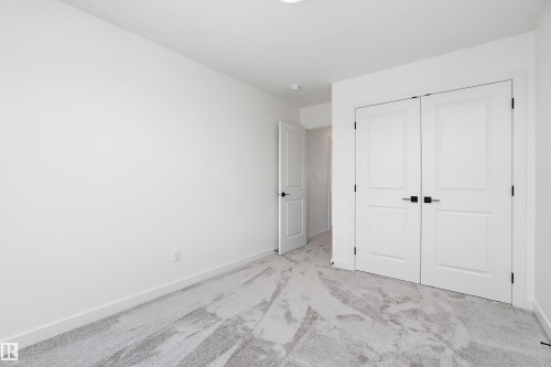 Light gray patterned carpeting, white walls, and white bi-fold doors with black hardware - 1763 Crossbill Loop Nw, Edmonton, AB - Indoor Photo Showing Other Room