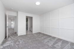 White panel accent wall, plush gray carpet, recessed lighting, white doors with matte black hardware, and a visible freestanding tub in a secondary space - 