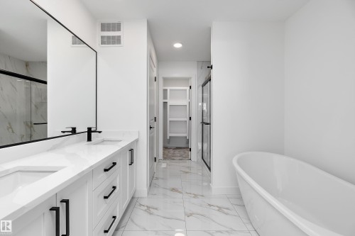 Dual vanity with white cabinetry and black hardware, freestanding soaking tub, frameless glass shower, and marble-look tile flooring - 1763 Crossbill Loop Nw, Edmonton, AB - Indoor Photo Showing Bathroom