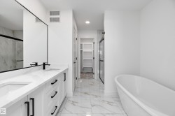 Dual vanity with white cabinetry and black hardware, freestanding soaking tub, frameless glass shower, and marble-look tile flooring - 