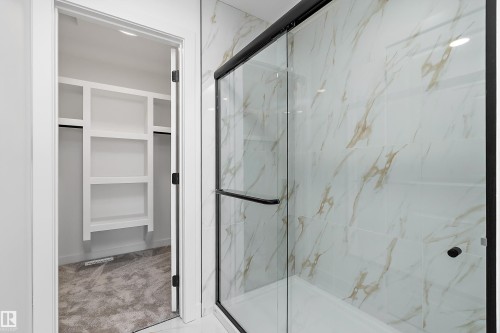 Shower enclosure with a clear glass sliding door, matte black frame, and white marble-look wall tiling - 1763 Crossbill Loop Nw, Edmonton, AB - Indoor Photo Showing Bathroom